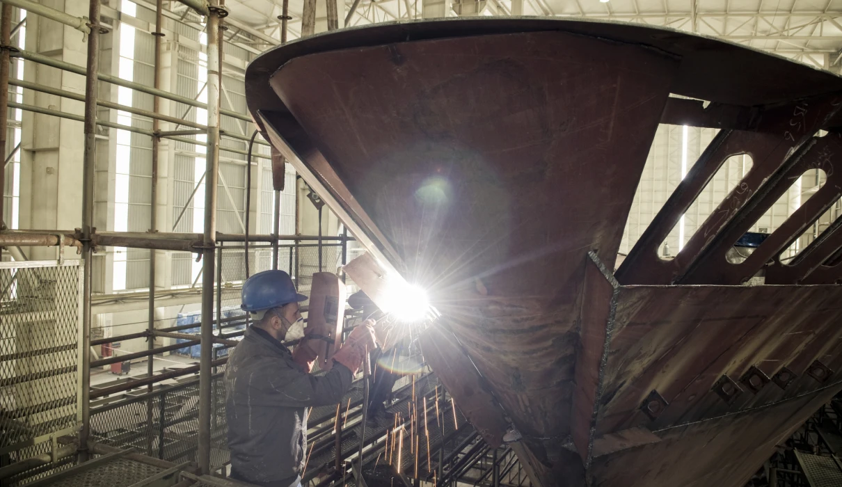 Worker welding ship hull in shipyard